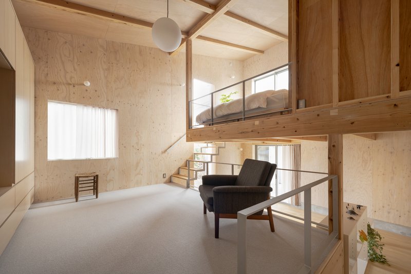 Double-height bedroom with vaulted plywood ceiling, suspended globe pendant, and upholstered lounge chair