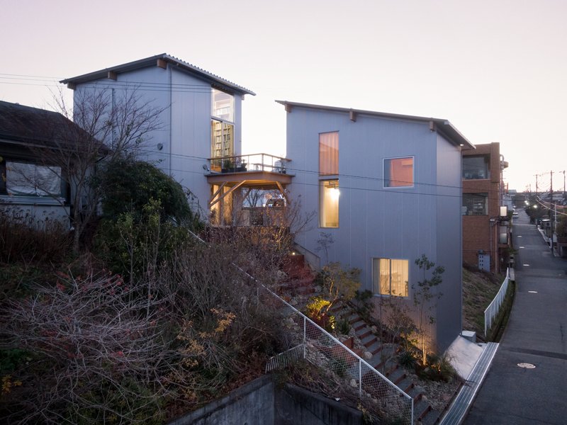 Hillside facade with corrugated metal cladding and illuminated windows at dusk overlooking a sloped landscape