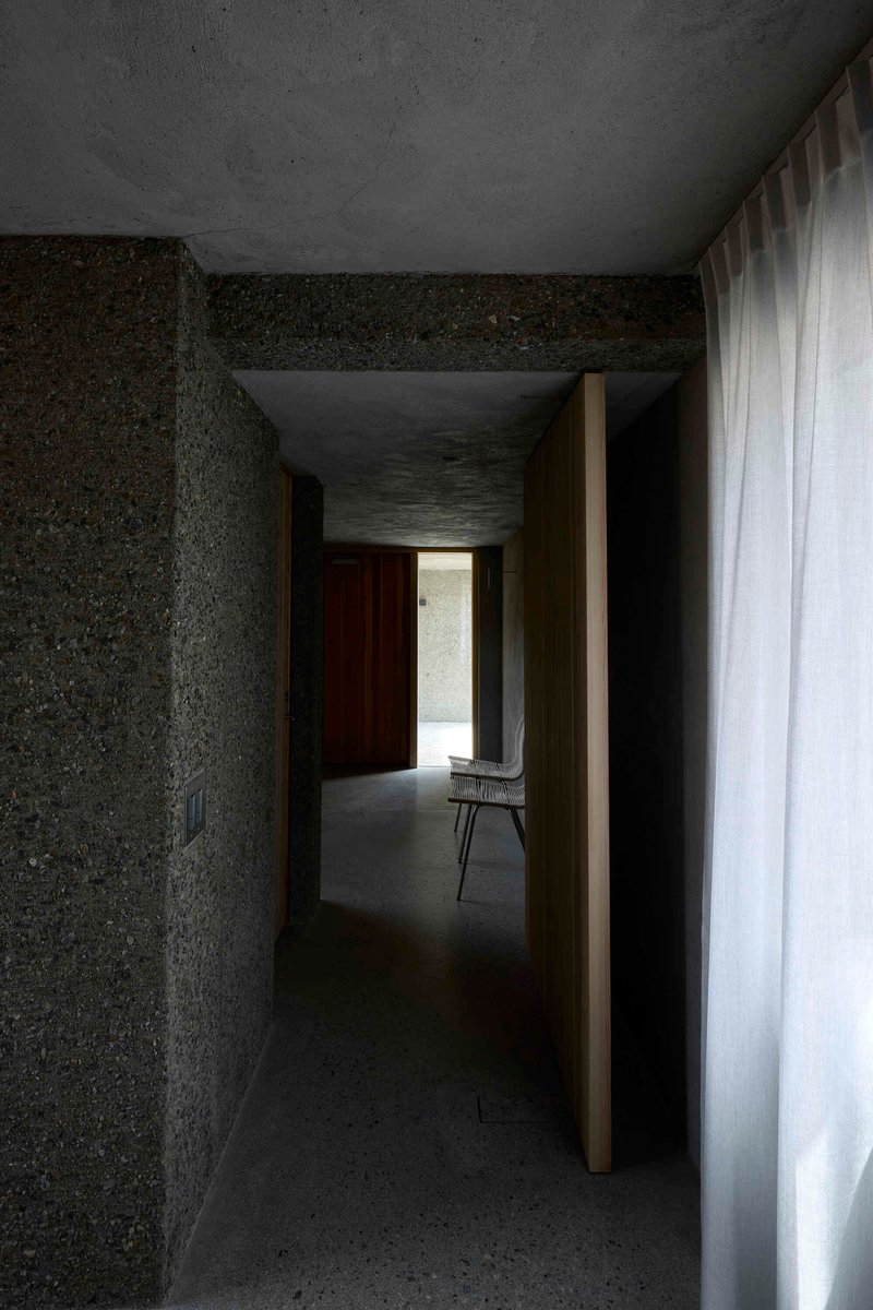 Concrete hallway with timber door jamb and chair silhouetted in daylit opening