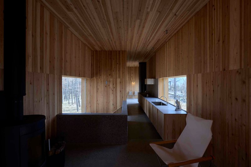 Kitchen and corridor with continuous timber surfaces and punched windows framing the winter forest
