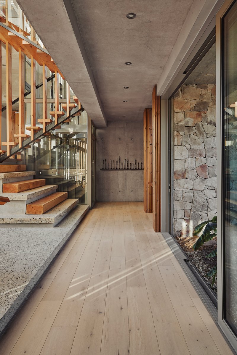 Interior corridor with pale timber flooring alongside open timber staircase and stone accent wall