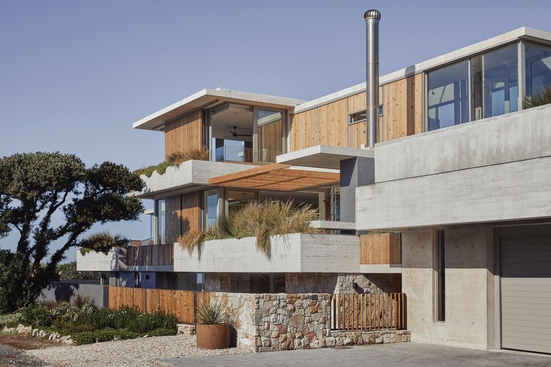 Multi-level facade combining concrete retaining walls, timber cladding and fieldstone masonry base with gravel forecourt