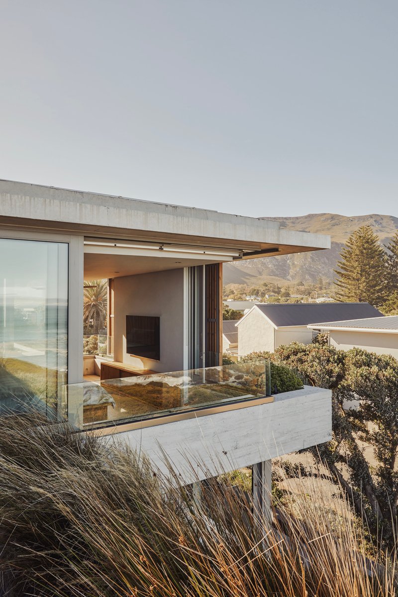Cantilevered concrete terrace with sliding glass doors opening to a living room, framed by coastal grasses