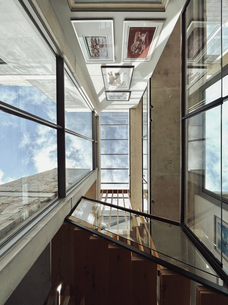 Upward view of a multi-story stairwell with skylights, timber treads and glass balustrades under blue sky