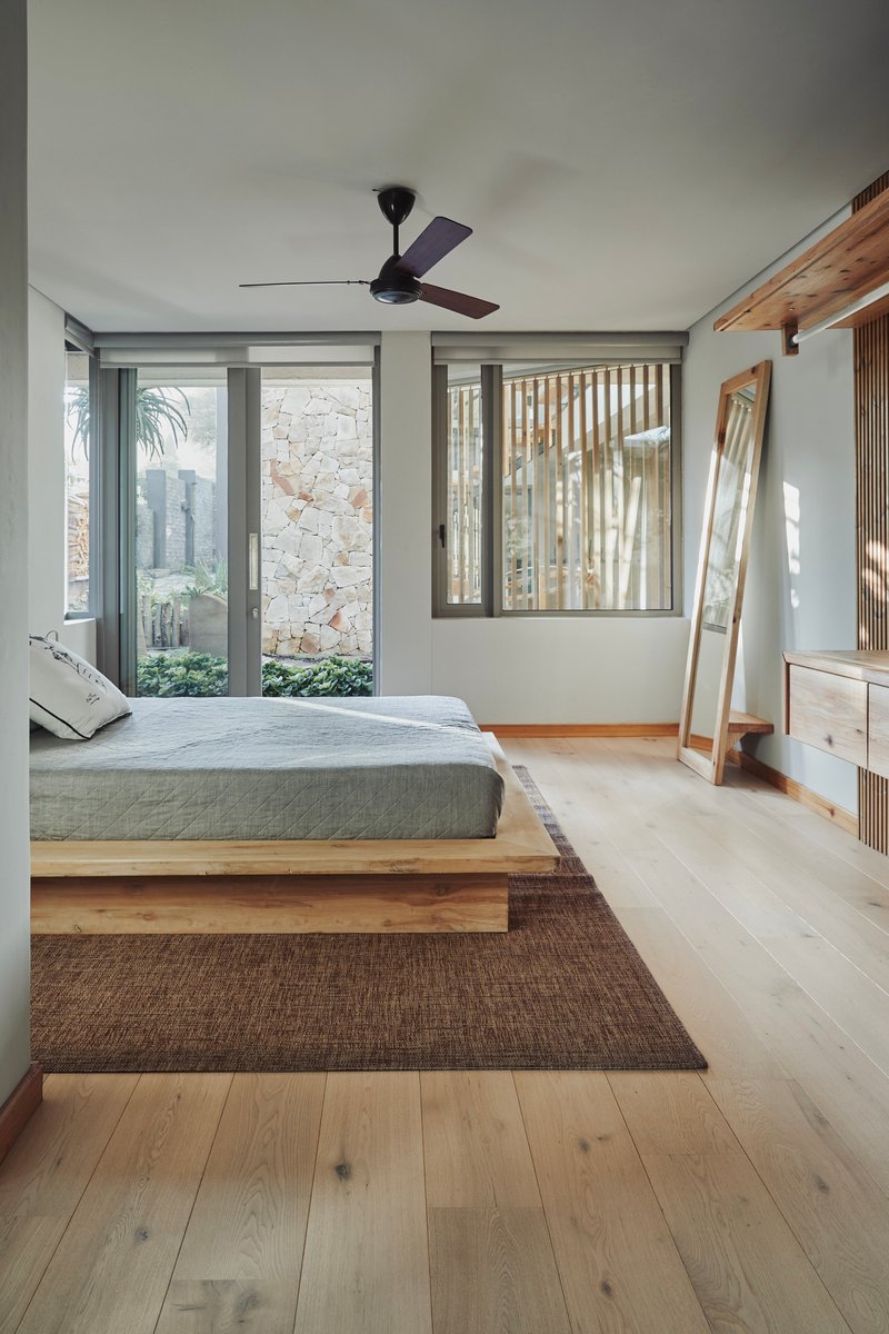 Bedroom with timber platform bed, ceiling fan and glass doors opening to a stone courtyard wall