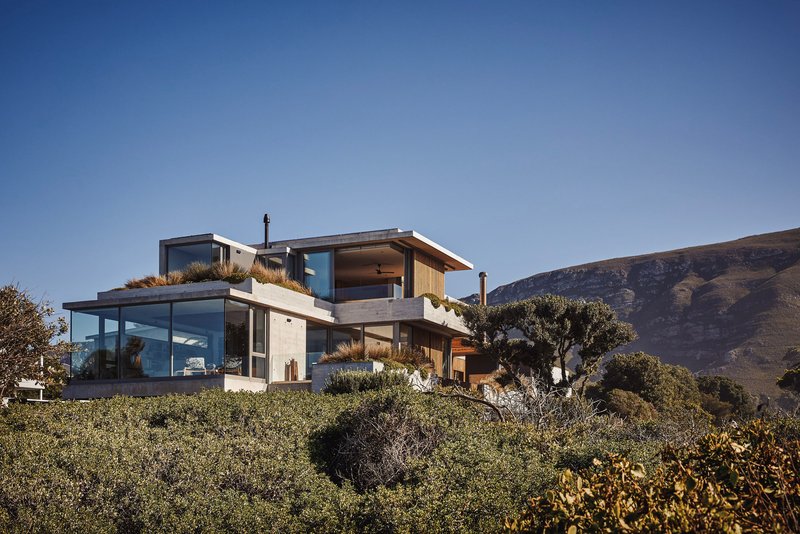 Terraced residence with concrete and timber volumes nestled into a vegetated hillside below distant mountains
