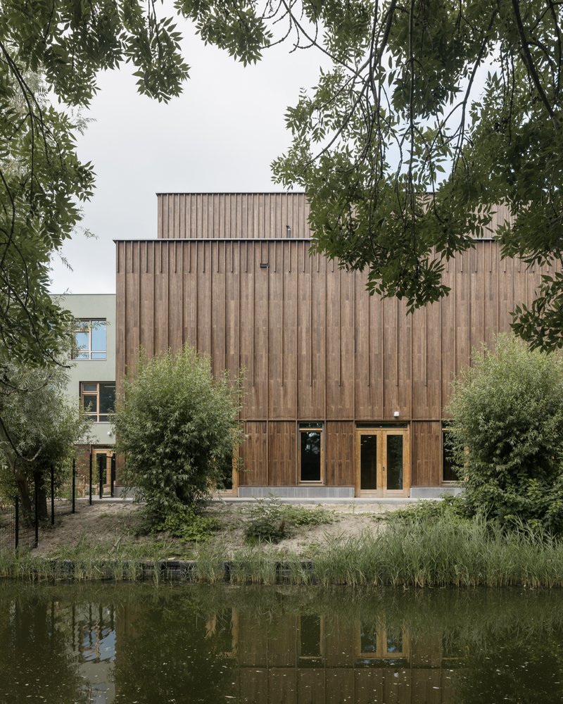 Rear elevation of the timber-clad volume reflected in a canal with overhanging tree branches framing the view