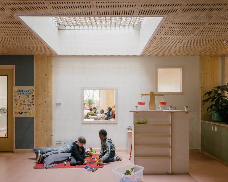 Interior room with perforated timber ceiling skylight and children playing on pink flooring below plywood shelving