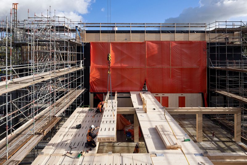 Construction site view showing red weatherproofing membrane and scaffolding surrounding timber structural frame