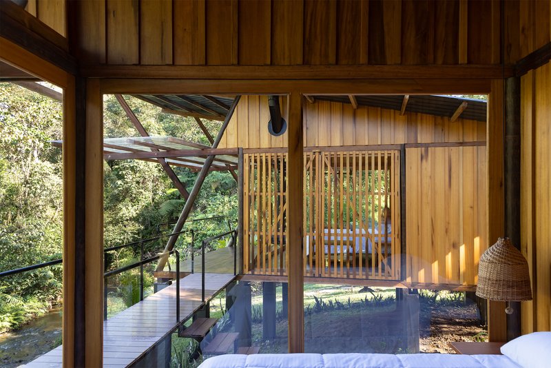 View from bedroom through timber-framed glazing to exterior walkway with diagonal bracing and forest beyond