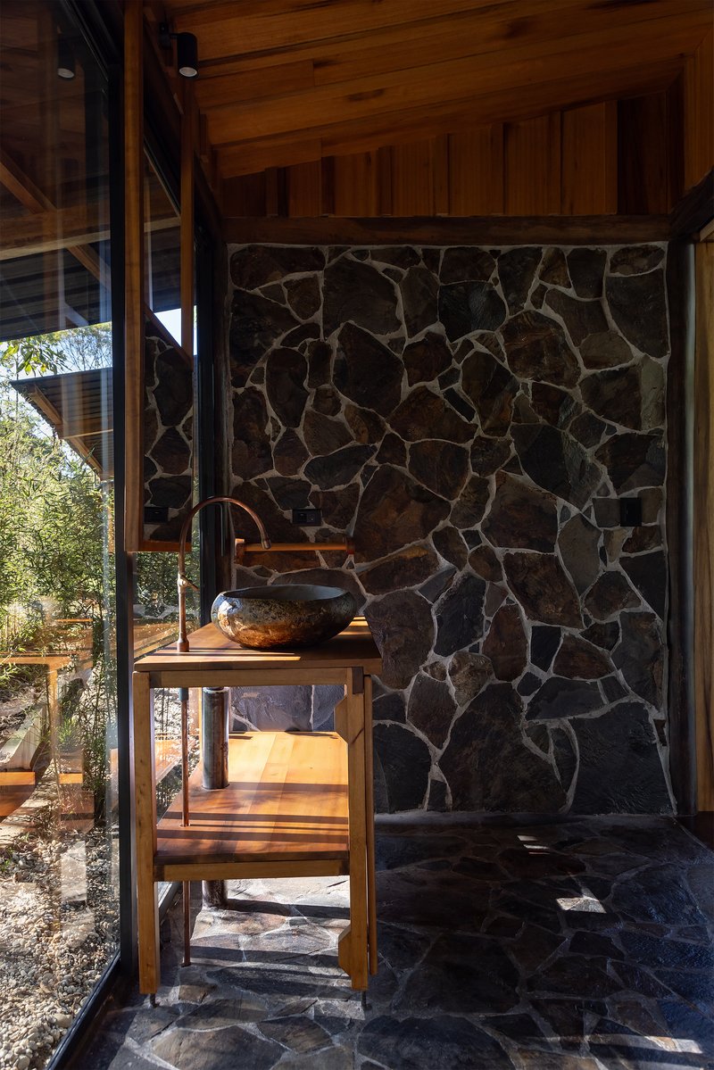 Interior view of dark stone wall with timber vanity and vessel sink beside floor-to-ceiling glass