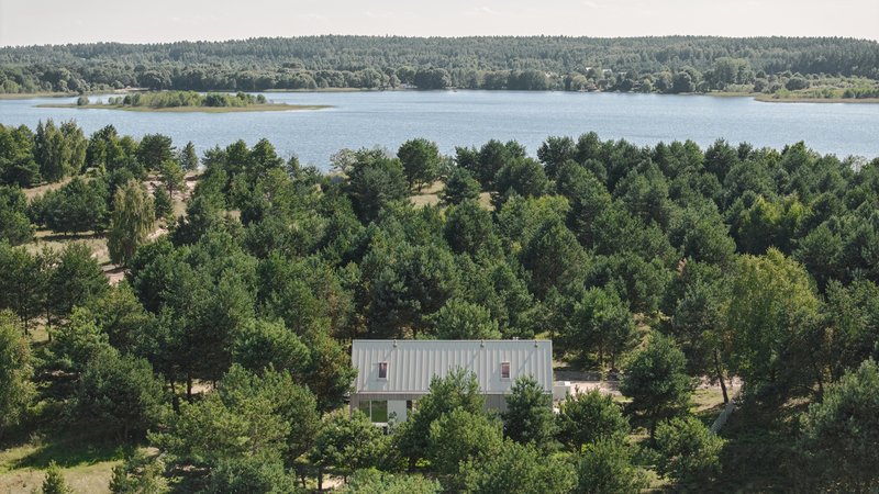 Aerial view of the gabled roof nestled among pine trees with a lake in the distance