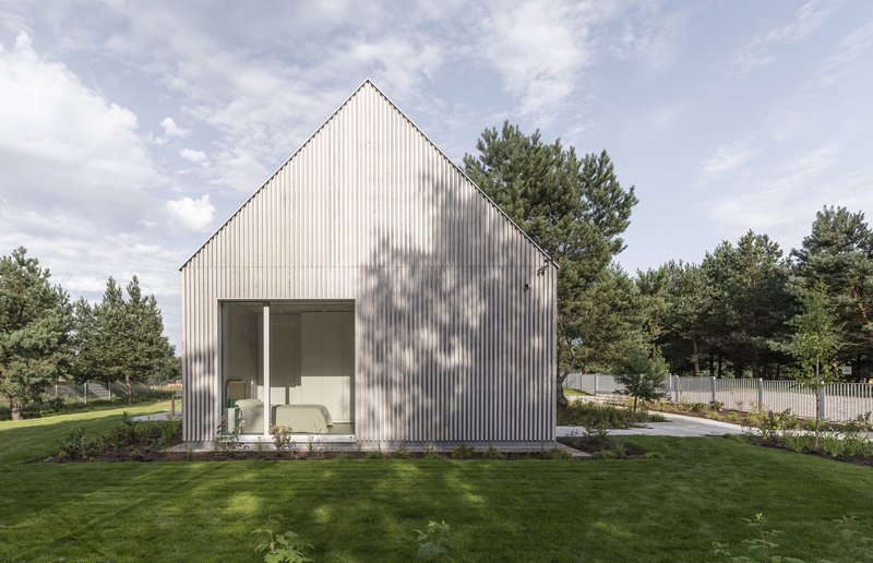 Garden elevation showing the corrugated metal cladding and recessed terrace with tree shadows on the facade