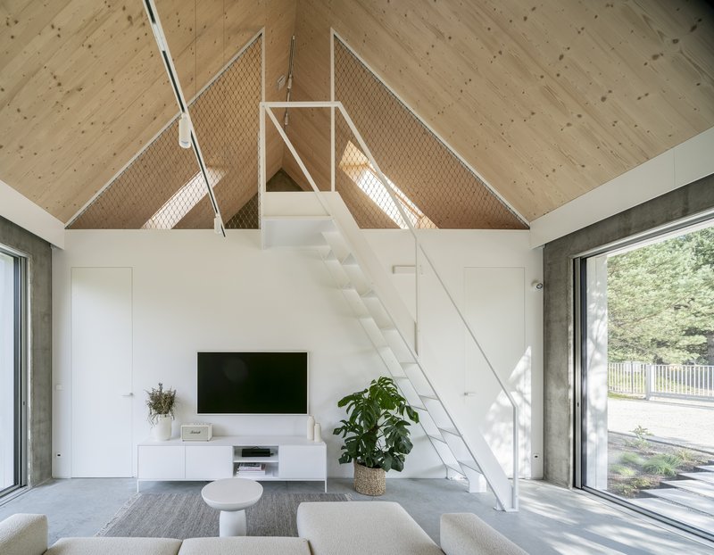 White metal stair beneath the vaulted plywood ceiling with mesh safety panels catching sunlight
