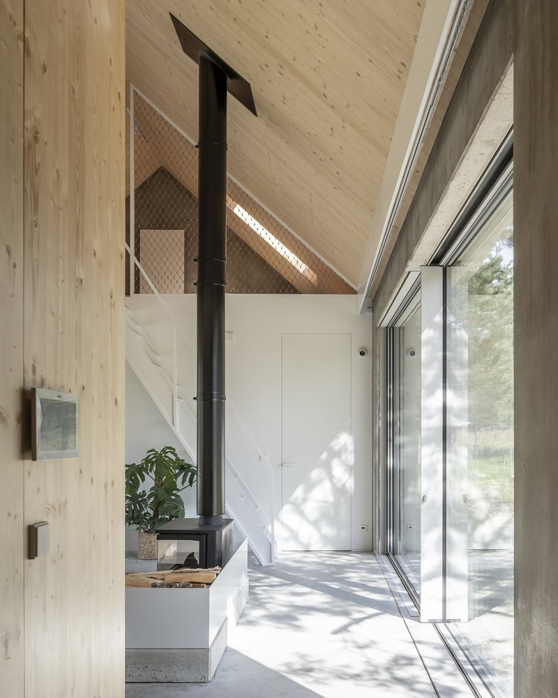 Double-height entry hall with black wood stove and mesh-screened loft under pitched timber ceiling