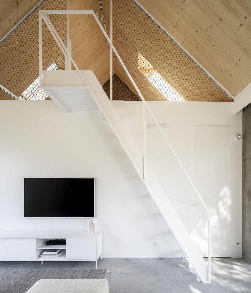 White steel staircase ascending to mezzanine level with wire mesh balustrade panels and timber ceiling