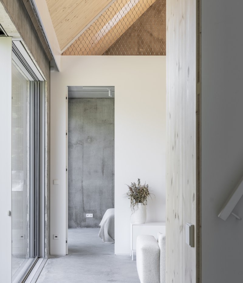 Hallway with polished concrete floor looking through to a bedroom framed by light timber columns