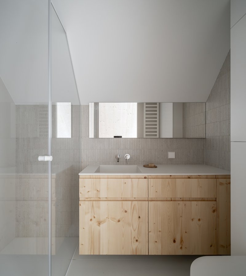Bathroom vanity with pale timber cabinetry below grey tile walls and a mirrored medicine cabinet