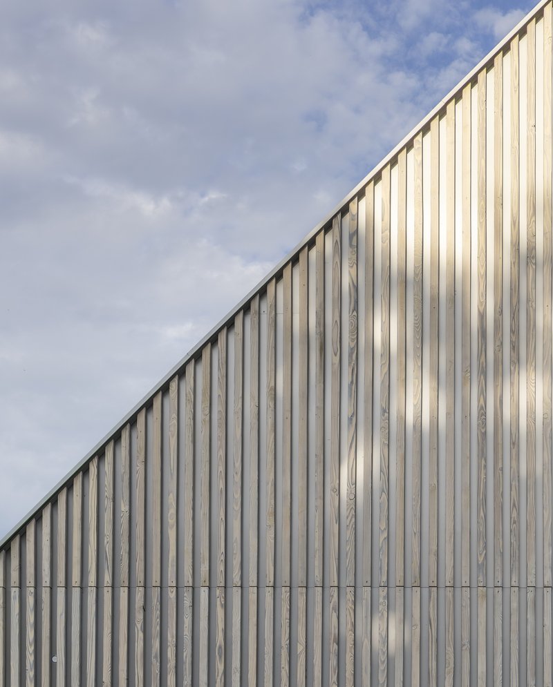 Vertical timber cladding facade sloping upward against a cloudy sky