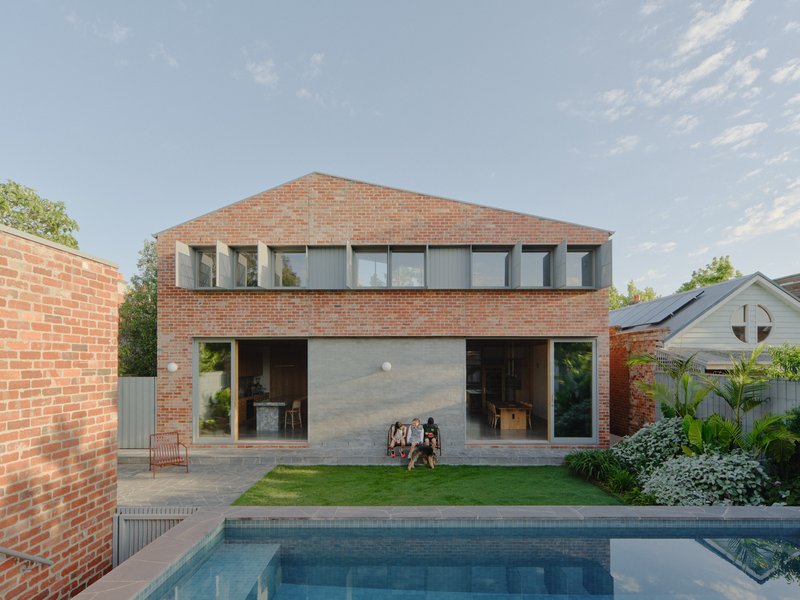 Rear facade with brick walls and continuous glazed opening overlooking a lawn and swimming pool