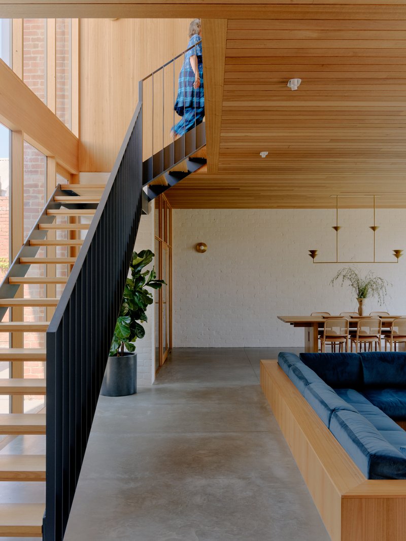 Black steel staircase with timber treads ascending past a timber-clad wall with a figure climbing