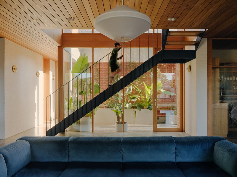 Black steel staircase with slender vertical balusters framing views to an outdoor courtyard with tropical plants
