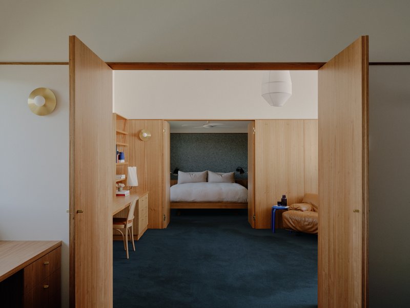 View through timber doorway into bedroom with dark upholstered headboard and paper pendant light