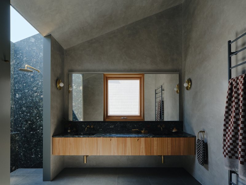 Bathroom vanity with black terrazzo countertop and timber cabinet beneath polished concrete ceiling and walls