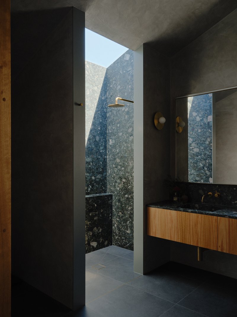 Open shower with speckled stone wall visible through doorway framed by grey concrete