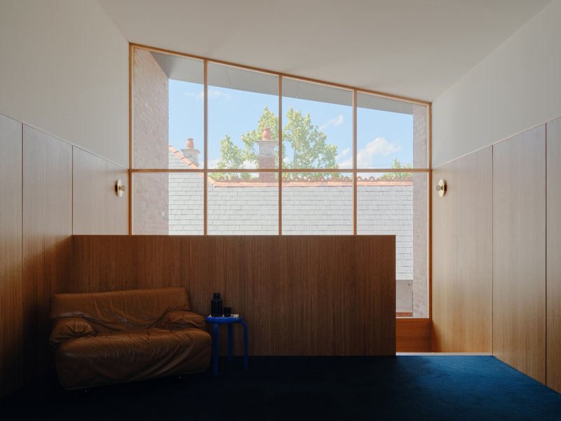 Floor-to-ceiling timber-framed window overlooking courtyard with white brick wall and tree