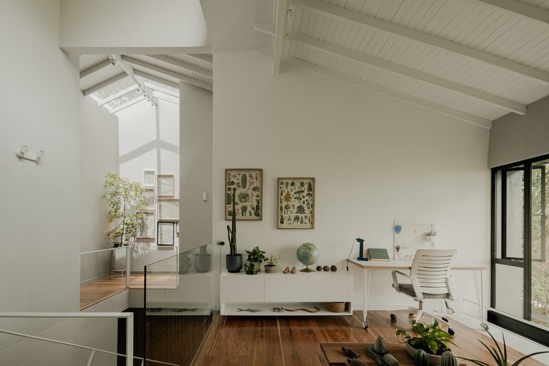 Upper level workspace with exposed white timber rafters and glass balustrade overlooking double-height void