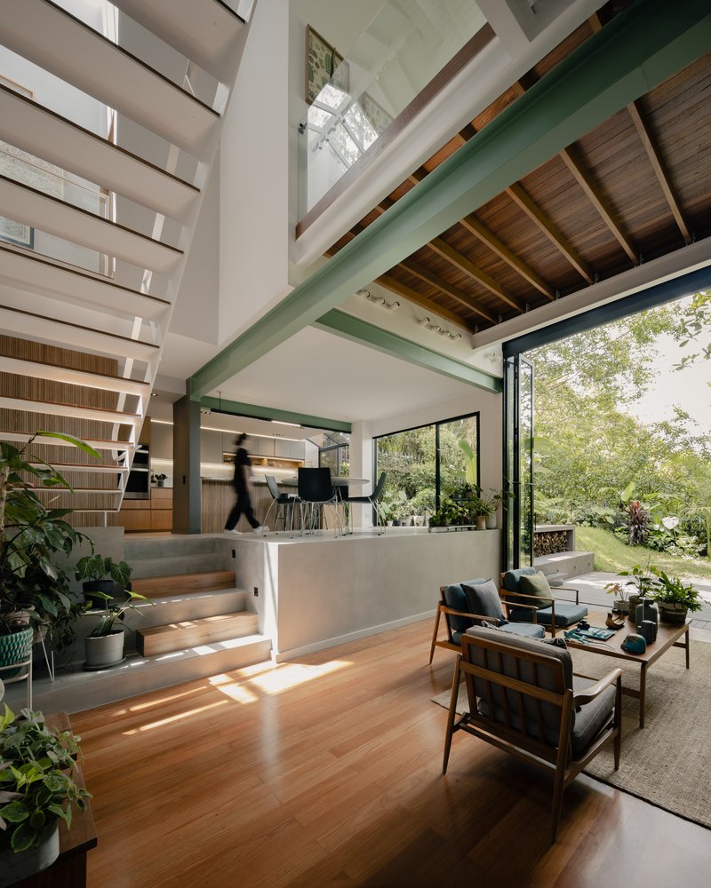 Double-height living space with green structural beams and open timber staircase flooded with natural light