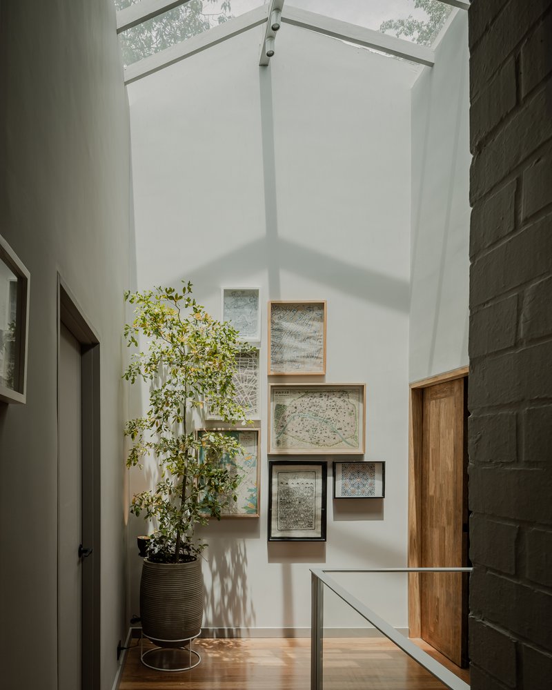 Double-height gallery wall with framed maps and timber niches lit by a corner skylight