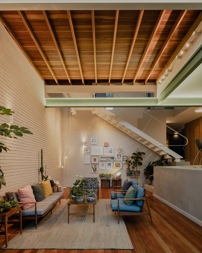 Living area beneath exposed timber ceiling joists with a steel-edged mezzanine and timber stair