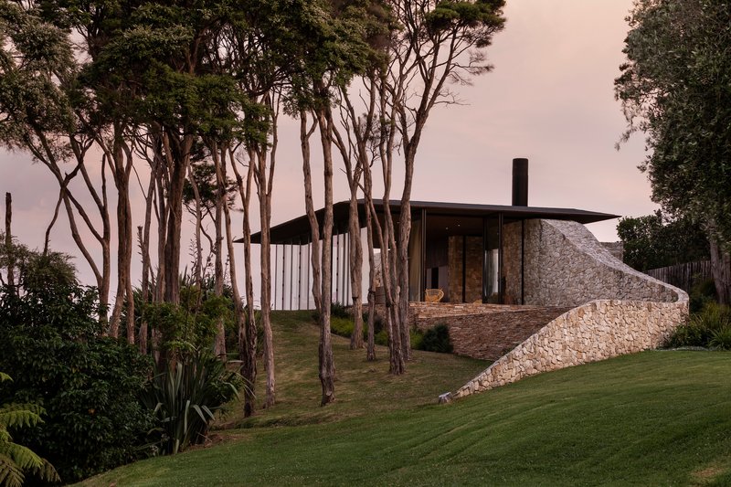 Hillside view of the stone and timber residence among slender trees under an overcast dusk sky