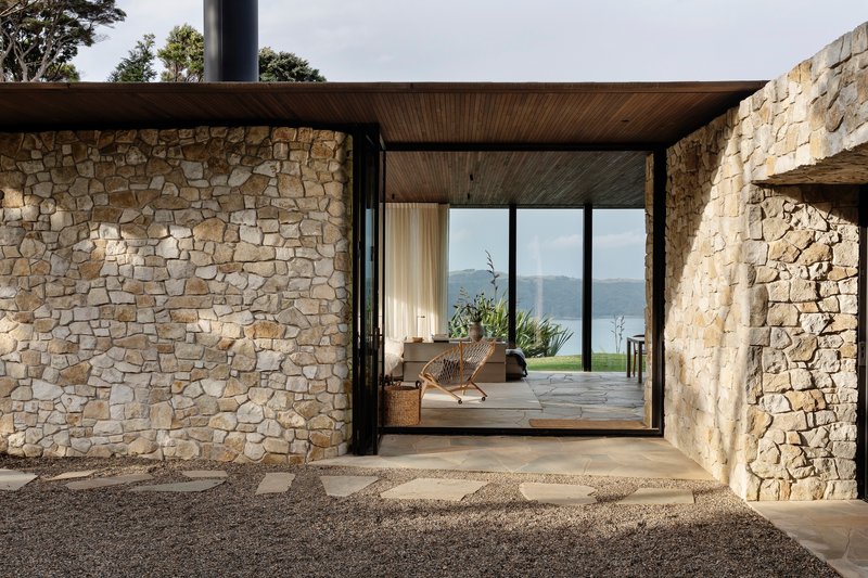 Covered entry breezeway with irregular stone walls and timber ceiling framing a view to distant water