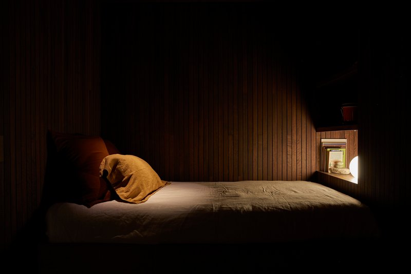 Bedroom at night with vertical timber wall cladding and a small illuminated window niche
