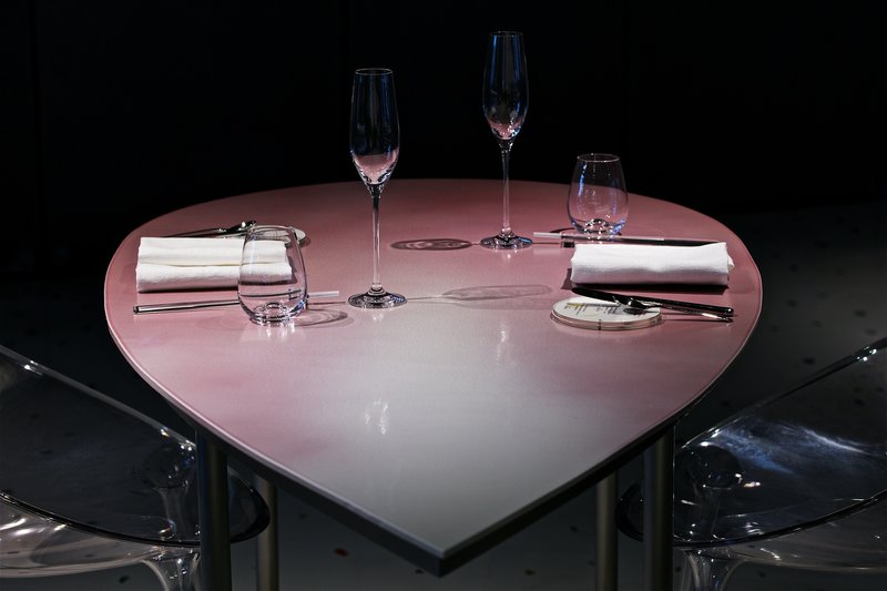 Heart-shaped pink table with place settings and glassware flanked by transparent acrylic chairs