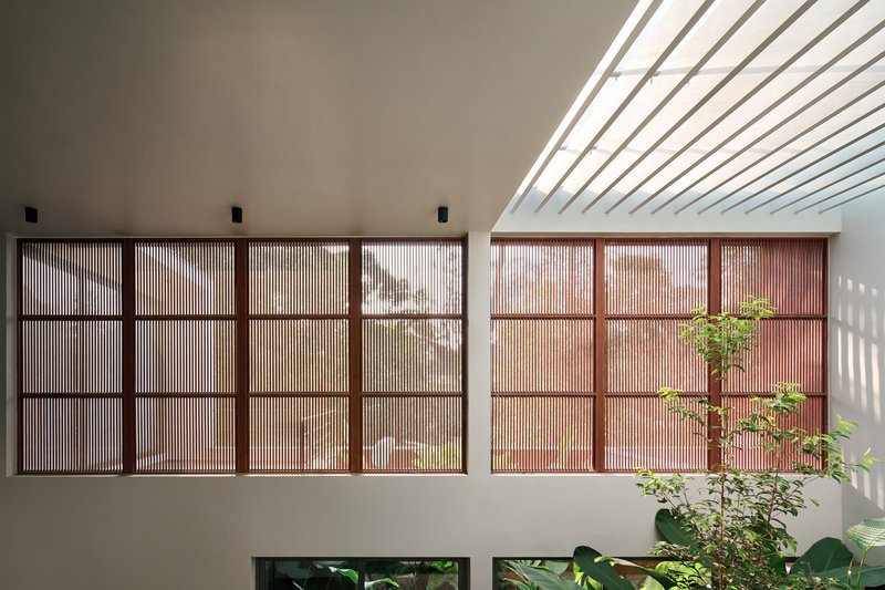 Timber-framed slatted screen wall with skylight above casting striped shadows across white surfaces