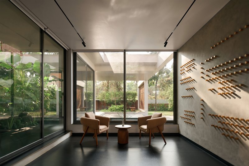 Interior seating alcove with floor-to-ceiling glazing overlooking a planted courtyard and perforated wall panels
