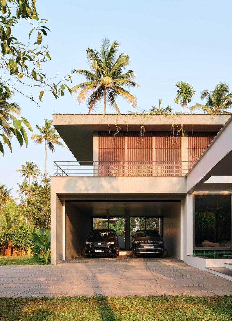 Ground level carport beneath a cantilevered terrace framed by vertical timber screens and palm canopy