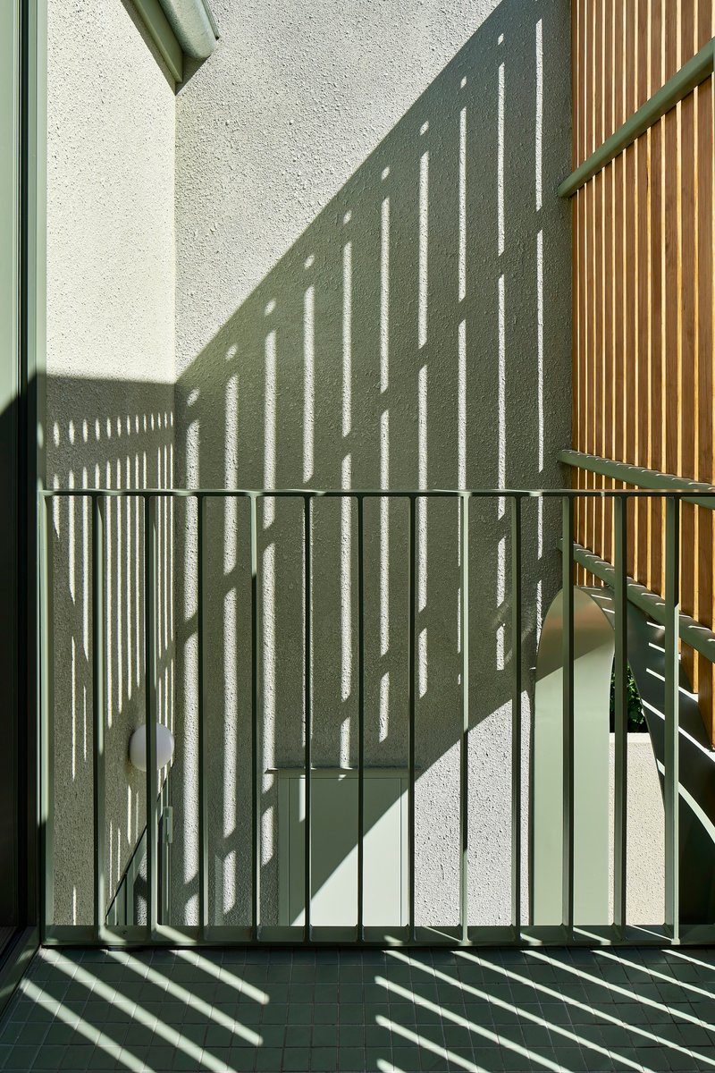 Green metal balustrade casting diagonal shadows on white wall and tiled floor in afternoon sun