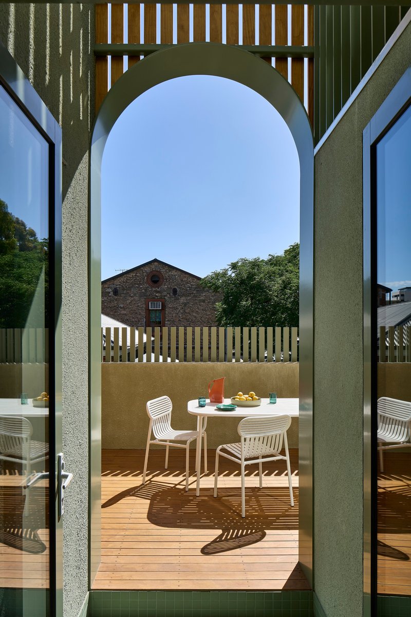 Arched doorway framing timber deck terrace with dining furniture and vertical slat screening