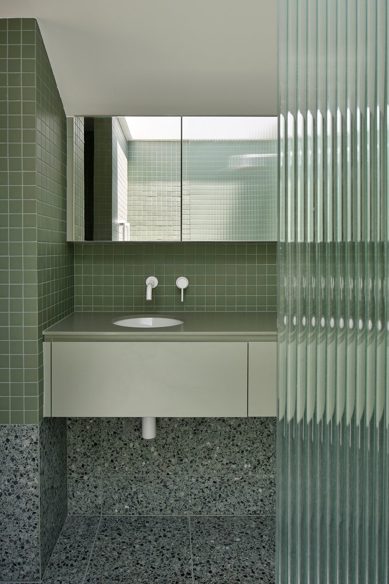 Bathroom with olive green square tile walls, terrazzo flooring, and vertical fluted glass screen beside floating vanity