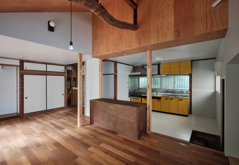 Living area with timber counter island overlooking a yellow kitchen beneath a vaulted wood ceiling