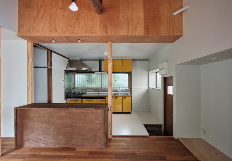 Timber counter with exposed columns framing view to yellow kitchen and suspended wood ceiling panel