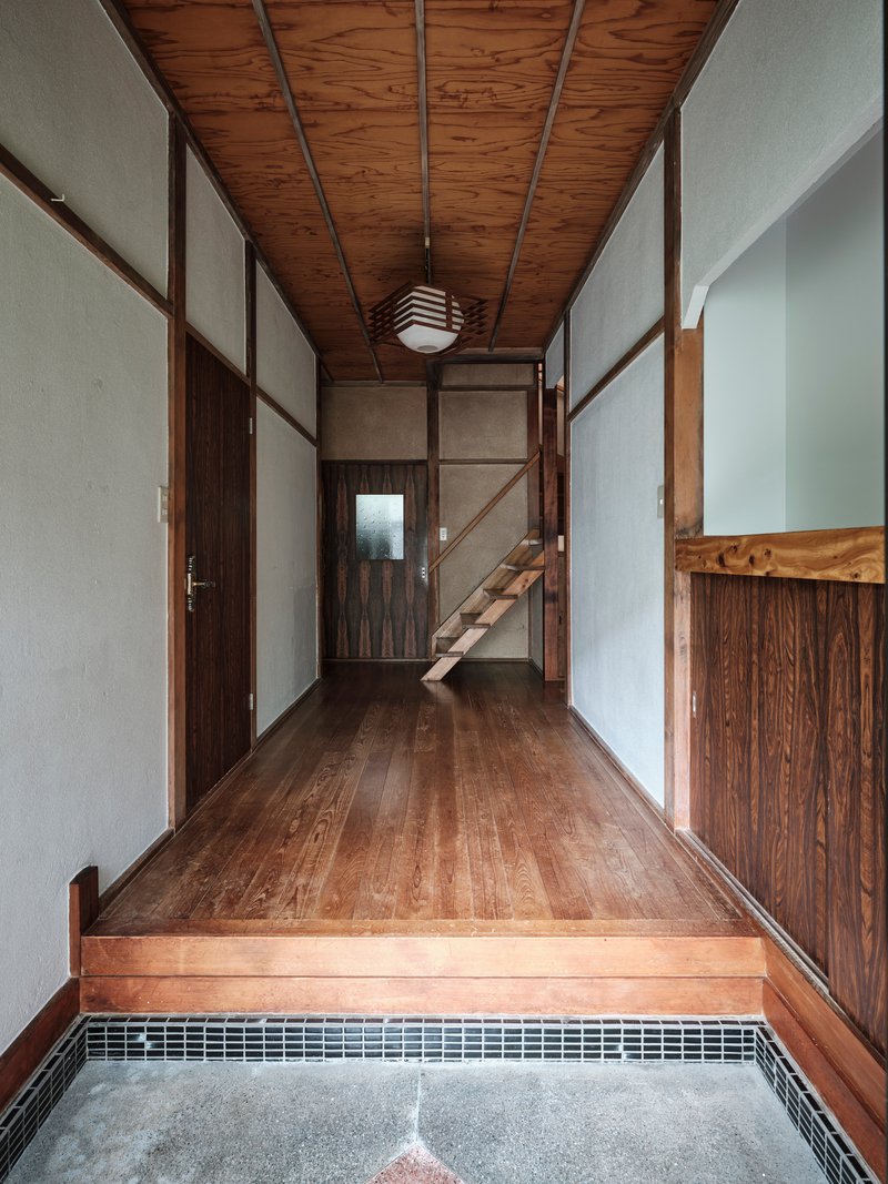 Entry hall with timber ceiling, paper walls, and a raised floor platform leading to an open staircase
