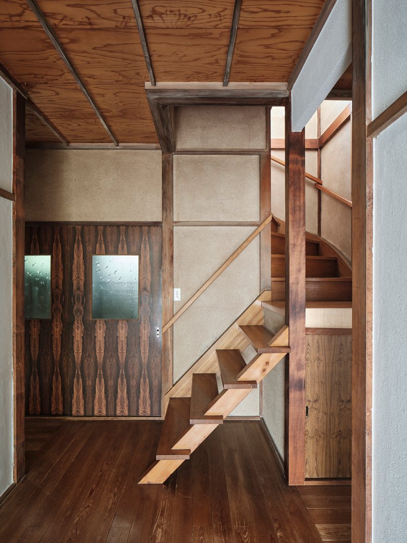 Open timber staircase rising against a textured plaster wall beneath an exposed beam ceiling