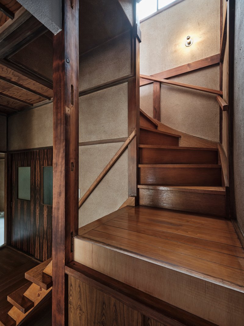 Timber staircase turning upward with wall sconce illuminating the textured plaster surface