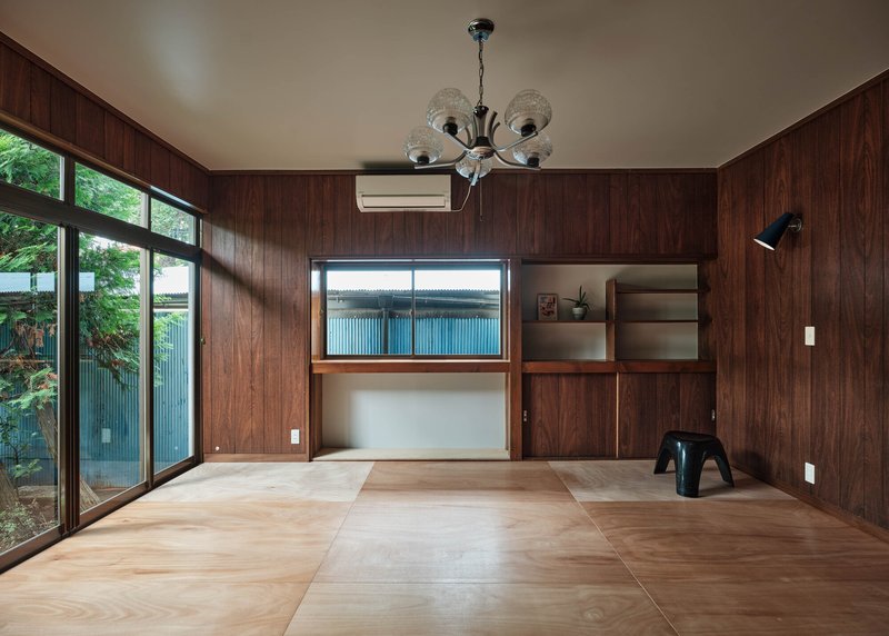 Tatami mat room with wood-paneled walls and glazed doors opening to garden foliage
